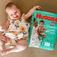A smiling baby in a white floral romper lies next to a pack of Huggies Newborn Zinc-Enriched Infant Nappies (Size 2, 4–8kg). The baby is reaching out joyfully, showcasing the product beside them. Social Soup Networker and Micro Creator Campaign.